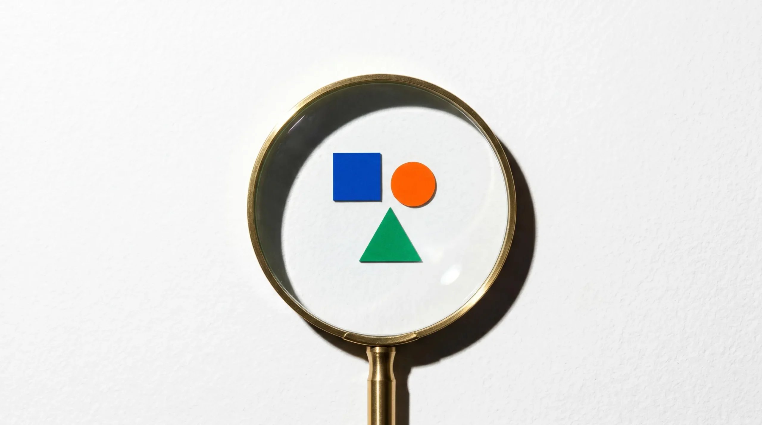 Loupe dorée posée sur surface blanche révélant motifs géométriques colorés symbolisant l'examen attentif des détails